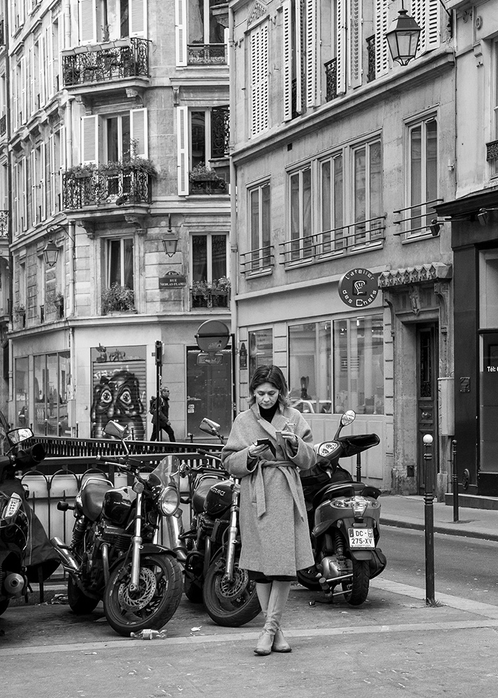 a woman smoking a cigarette and drinking coffee on a street at Paris
